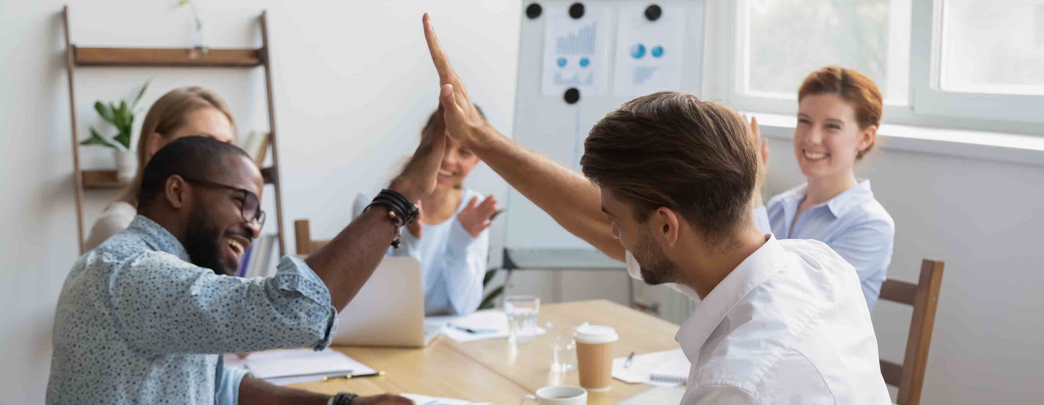 Happy diverse male colleagues join hands giving high five celebrating shared win successful teamwork result at group office meeting get team support, congratulate with job well done victory reward